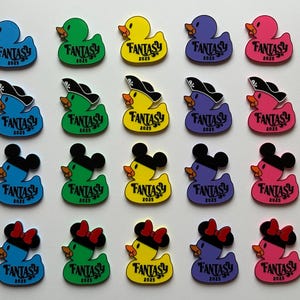 May include: A collection of colorful duck-shaped pins. Each pin features the word "FANTASY" and the year "2025". Some ducks have pirate hats, Mickey Mouse ears, or Minnie Mouse bows. Colors include blue, green, yellow, purple, and pink.
