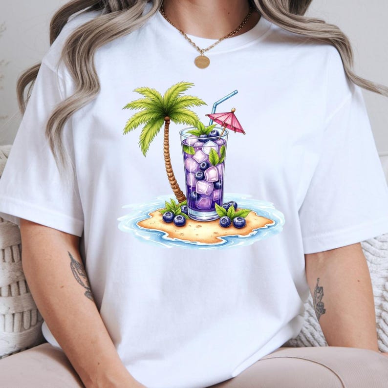 May include: A white t-shirt featuring a graphic print of a tall glass filled with a purple blueberry beverage, ice cubes, and a small pink cocktail umbrella. Next to the glass is a palm tree on a small sandy island surrounded by blue water.