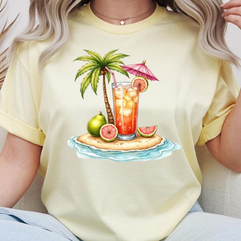 May include: A pale yellow t-shirt featuring a graphic of a tropical island scene. The design includes a palm tree, a glass of iced orange beverage with a pink umbrella, a green pear, and sliced grapefruit segments on a sandy beach with blue water.