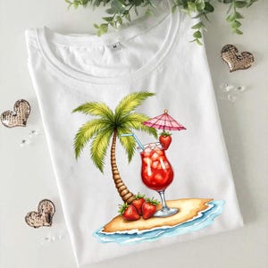 May include: A white t-shirt featuring a graphic of a tropical island with a palm tree, a red strawberry cocktail in a glass with a blue straw and a pink umbrella, and two fresh strawberries resting on the sand near the water's edge.
