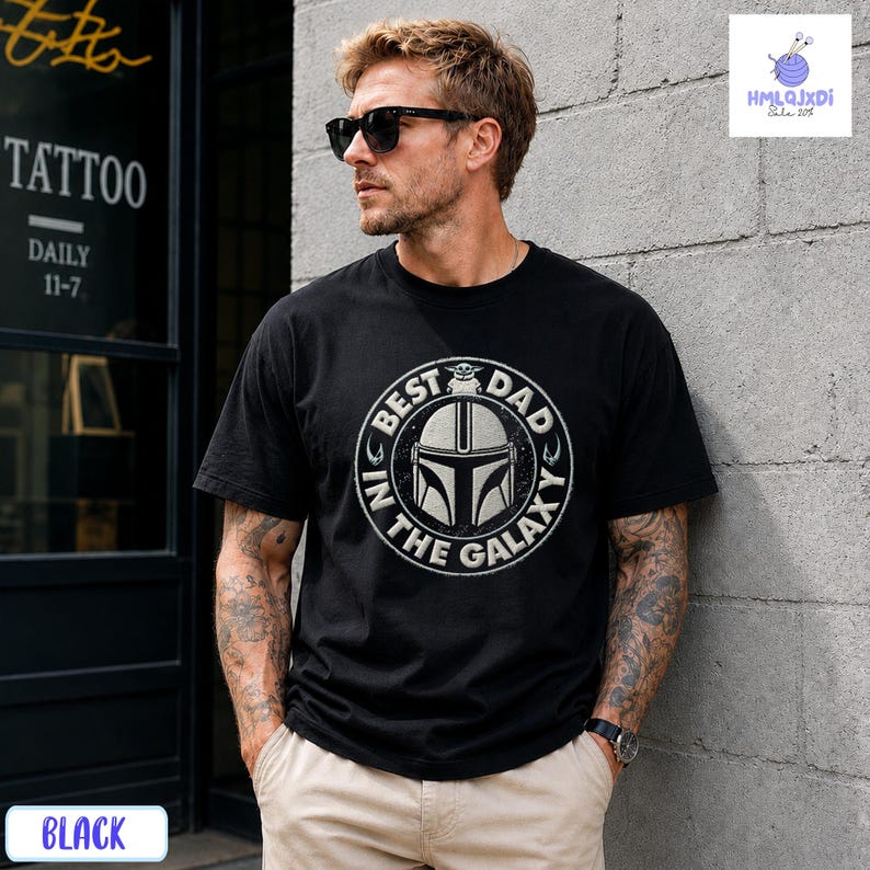 A man wearing a black t-shirt with a graphic design stands in front of a tattoo shop.