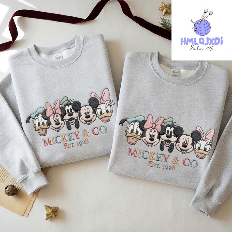 two gray sweatshirts with a group of Disney characters, including Mickey Mouse, Donald Duck, Goofy, and Minnie Mouse, printed on them. The sweatshirts are displayed on a white surface, with a red ribbon and some decorations in the background.