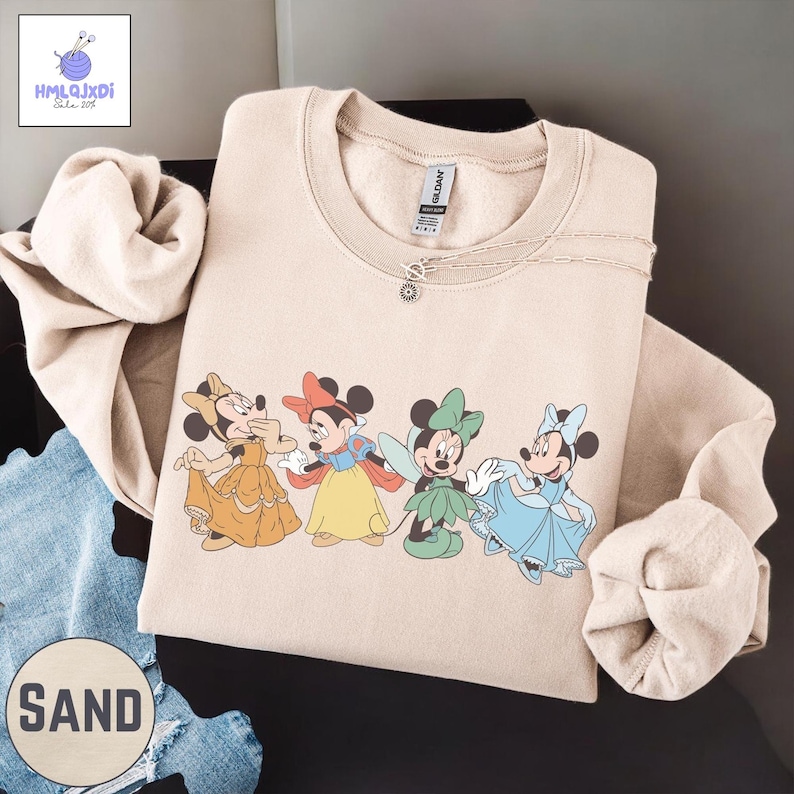 A beige sweatshirt with a graphic of four Disney Minnie Mouse characters, including Snow White and the Seven Dwarfs, printed on it.