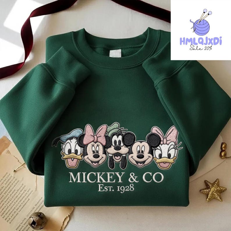 A green sweatshirt with a graphic design featuring the faces of Disney characters Mickey Mouse, Minnie Mouse, Donald Duck, Goofy, and Pluto, along with the text "MICKEY & CO Est. 1928".