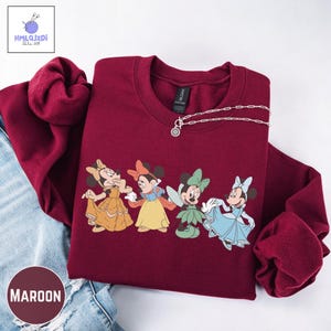 A red sweater with a graphic of four Disney Minnie Mouse characters, including Snow White and the Seven Dwarfs, printed on it.