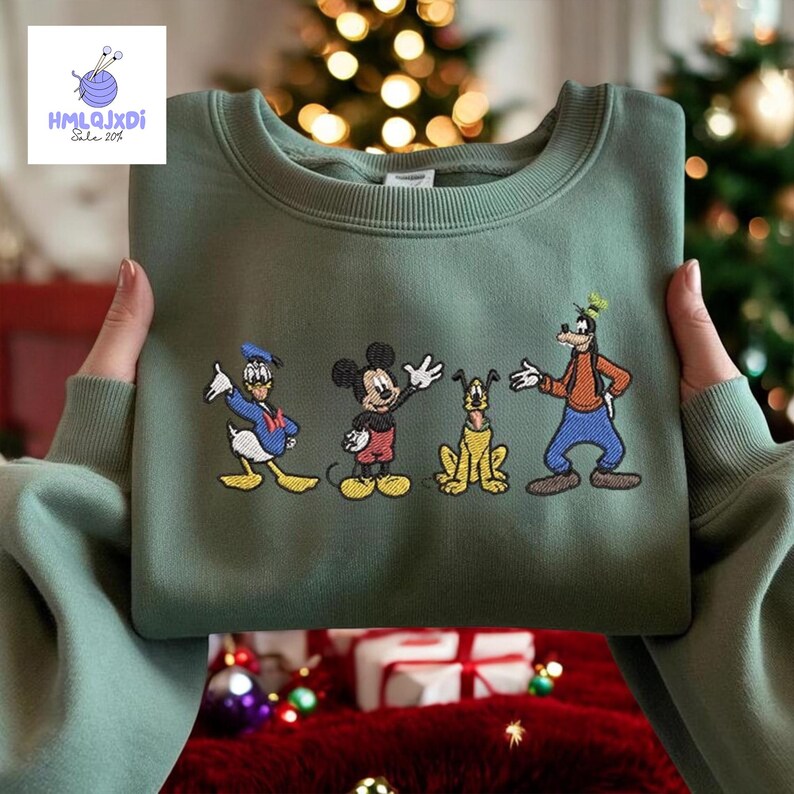 A person is holding up a green sweater with a design of Disney characters, including Mickey Mouse, Donald Duck, Goofy, and Pluto, against a background of Christmas lights and a decorated tree.