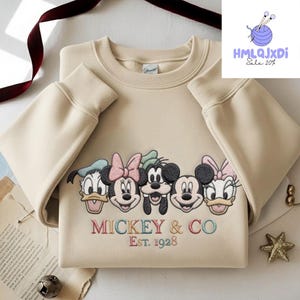 A beige sweater with a graphic design featuring the faces of Disney characters Mickey Mouse and Co.