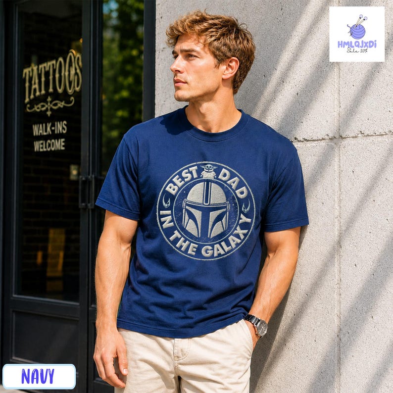 A man wearing a navy blue t-shirt with a graphic design stands in front of a tattoo shop.