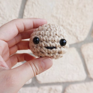 May include: A small crocheted brown toy with black eyes and a smiling mouth.