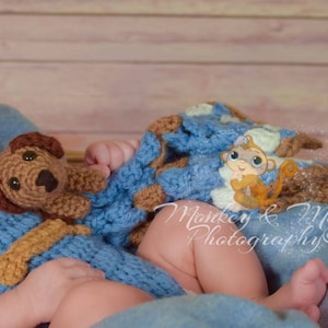 Pu&ograve; includere: Un bambino &egrave; avvolto in una coperta all'uncinetto blu e marrone con un giocattolo di cane all'uncinetto marrone e un'illustrazione di scimmia dei cartoni animati. Il testo "Monkey & Me Photography" &egrave; visibile nell'immagine.