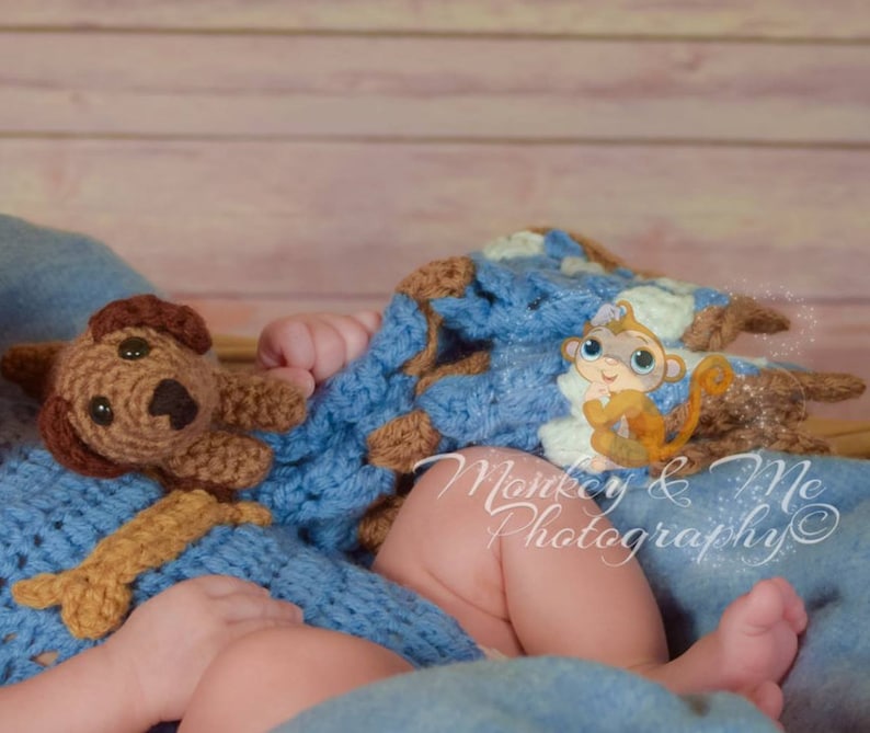 Pu&ograve; includere: Un bambino &egrave; avvolto in una coperta all'uncinetto blu e marrone con un giocattolo di cane all'uncinetto marrone e un'illustrazione di scimmia dei cartoni animati. Il testo "Monkey & Me Photography" &egrave; visibile nell'immagine.