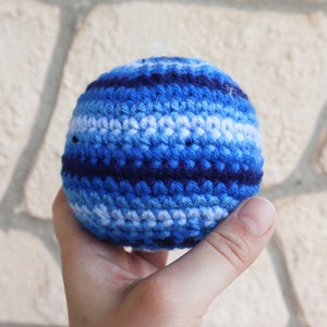 May include: A blue, white, and navy blue crocheted ball. The ball is made of yarn and has a striped pattern.