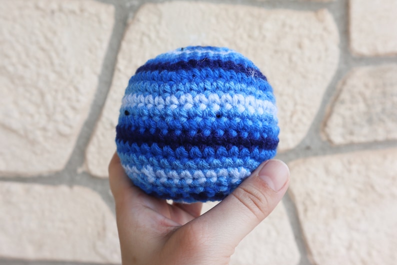 May include: A blue, white, and navy blue crocheted ball. The ball is made of yarn and has a striped pattern.