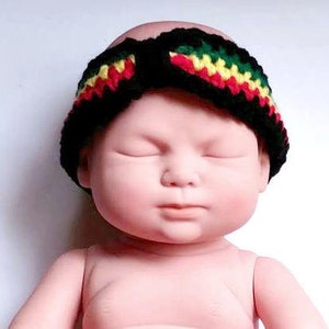 May include: A black crochet headband with red, yellow, and green stripes. The headband is worn by a doll. The headband is a baby accessory.