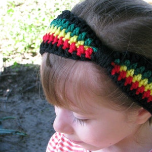 May include: A black crochet headband with green, yellow, and red stripes. The headband is worn on a person's head. The colors are arranged in a pattern, creating a vibrant and eye-catching accessory. The headband is a handmade item.