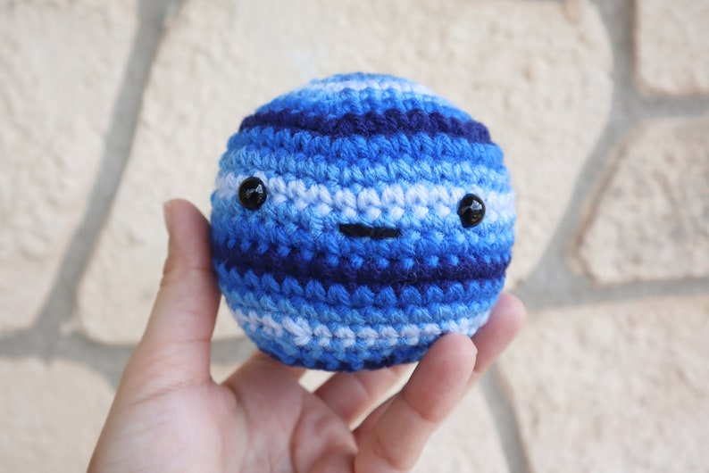 May include: A blue and white crocheted ball with a smiling face. The ball has black eyes and a stitched-on mouth.