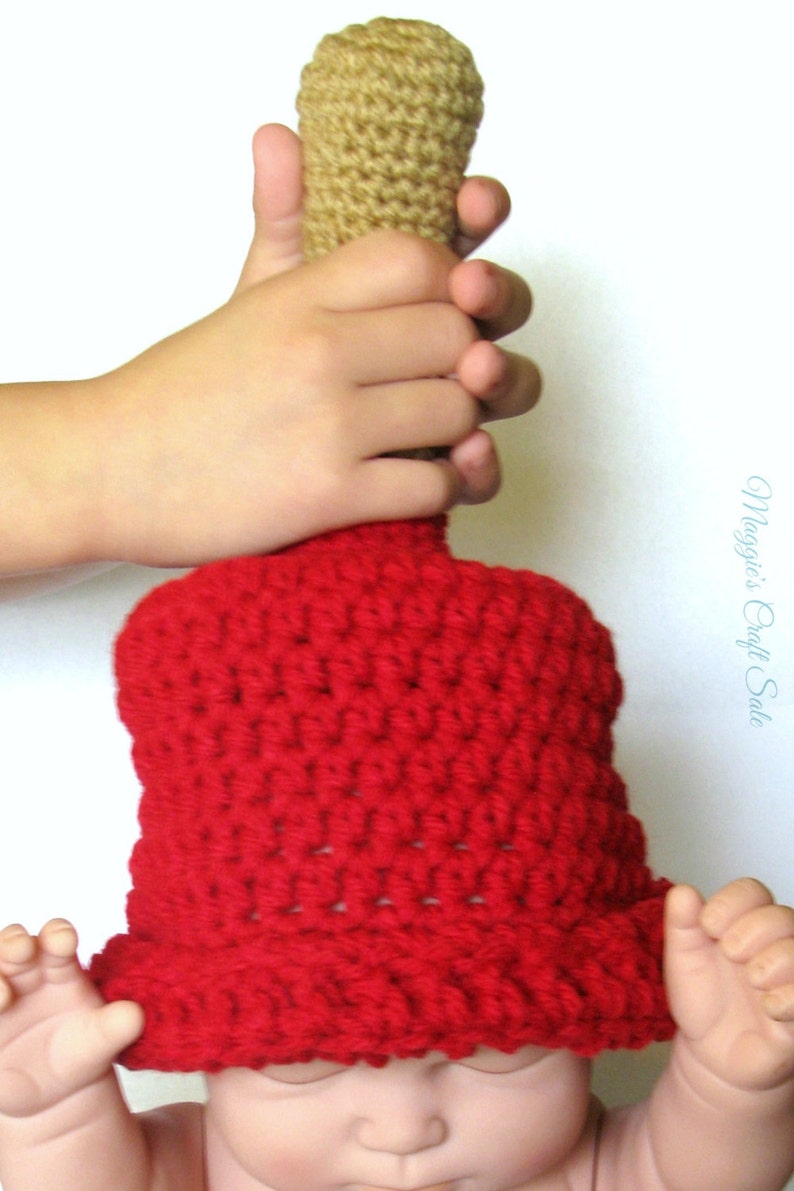 Puede incluir: Un gorro de punto rojo con una parte superior de punto marr&oacute;n. El gorro est&aacute; siendo sostenido por una mano.