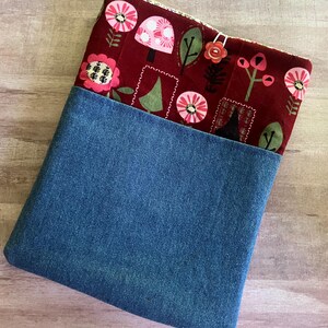 May include: A denim and fabric pouch with a whimsical floral design. The top section features a deep red fabric adorned with pink flowers, mushrooms, and green leaves. The bottom half is made of blue denim.