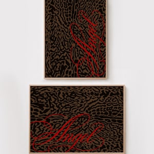 May include: Two framed wall art pieces featuring a brown and black animal print pattern. Each print displays the word Angel written in a bright red, cursive script font. The frames are made of a light-colored wood, providing a clean border.