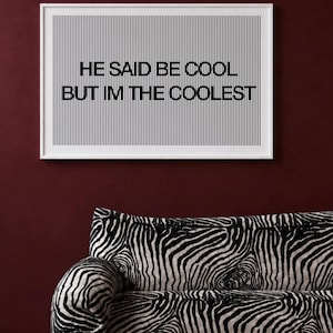 Könnte beinhalten: Ein rechteckiger Wandkunstdruck in einem weißen Rahmen mit vertikalen schwarzen Linien auf weißem Hintergrund und dem schwarzen Text HE SAID BE COOL BUT IM THE COOLEST in der Mitte des Drucks, platziert über einem Sofa mit Zebramuster.