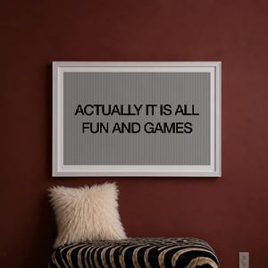 Peut inclure: Une œuvre d'art murale rectangulaire dans un cadre blanc présentant un fond à rayures verticales noires et blanches avec le texte ACTUALLY IT IS ALL FUN AND GAMES imprimé en lettres capitales noires grasses au centre du motif rayé.