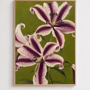 May include: A framed botanical painting featuring two large, open lily flowers with white petals, deep purple central stripes, and dark purple speckles. The flowers are set against a solid, muted olive green background, enclosed in a light wood frame.