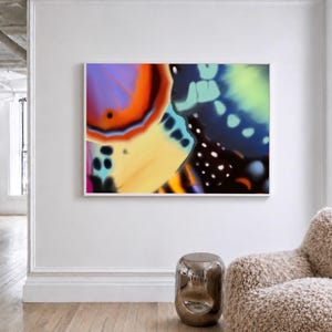 May include: A framed abstract art print featuring a close-up of a butterfly's wing. The artwork showcases vibrant colors including purple, orange, yellow, and blue, with intricate patterns and details. The print is displayed in a white frame.