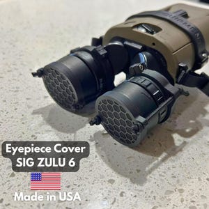 May include: An eyepiece cover for SIG ZULU 6 night vision device. The device is olive drab with black eyepieces and a black strap. The eyepieces have a honeycomb pattern. The text "Eyepiece Cover SIG ZULU 6" is visible.