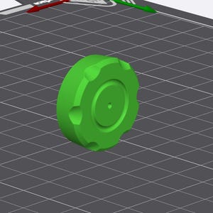 May include: A bright green, circular object with a ridged edge and a central indentation. The object is positioned on a gray grid, with directional arrows and a measurement line visible in the background. The object appears to be a 3D-printed component.