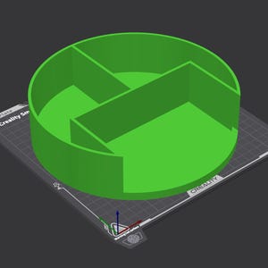 以下が含まれることがあります： 内部に仕切りがある、鮮やかな緑色の円形3Dプリントオブジェクト。おそらく収納容器またはオーガナイザー。グレーの表面に配置され、「Creality Sm」の文字とその他の技術的なマーキングがあります。デザインは幾何学的でモダンです。