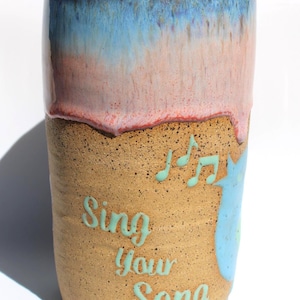 May include: A set of three ceramic mugs with a speckled, matte finish. The mugs are in shades of cream, light gray, and dark gray. Each mug has a simple, minimalist design, perfect for coffee or tea.