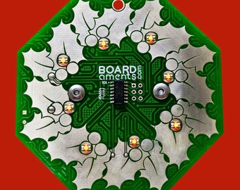 May include: A green circuit board in an octagonal shape with a holly leaf design. The board has the text "BOARDS ements q.com" and several small lights. The background is a solid red color.
