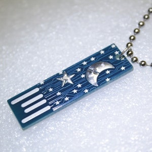 May include: A blue rectangular pendant necklace with a circuit board design. The pendant features a silver crescent moon and star, with additional white stars. The necklace has a silver ball chain.