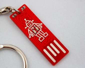 May include: Red USB flash drive with a robot design. The rectangular drive has a silver keyring attachment. The robot is white and has a simple, geometric design. The drive has white stripes at the end.