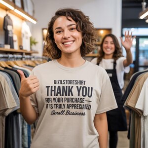 A smiling woman wearing a t-shirt with text, standing in a clothing store with another woman waving at her.