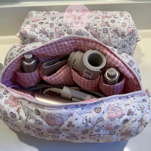 May include: A quilted cosmetic bag with a pink and white teddy bear pattern, open to reveal medical equipment. The interior features a pink gingham lining and pockets. Another bag is visible in the background.