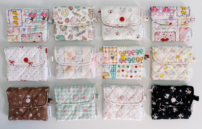 May include: A collection of quilted fabric pouches in various patterns and colors. Designs include floral, polka dots, and cartoon characters. Each pouch has a button closure and a small loop. The pouches are arranged in a grid.