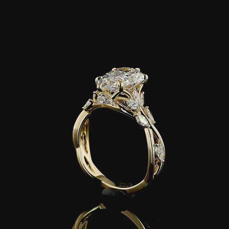 Puede incluir: Un anillo de compromiso de oro con una gran piedra central de diamante de talla ovalada. El anillo presenta diamantes de acento m&aacute;s peque&ntilde;os y una banda decorativa. El anillo est&aacute; sobre un fondo negro.
