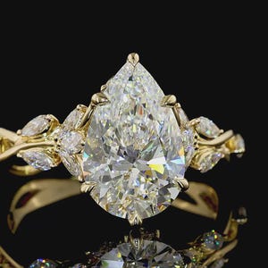 Puede incluir: Un anillo de oro con un gran diamante en forma de pera como pieza central. El anillo est&aacute; adornado con diamantes m&aacute;s peque&ntilde;os con corte marquesa y detalles intrincados en oro, creando un dise&ntilde;o lujoso y elegante. La banda del anillo tiene un dise&ntilde;o floral.