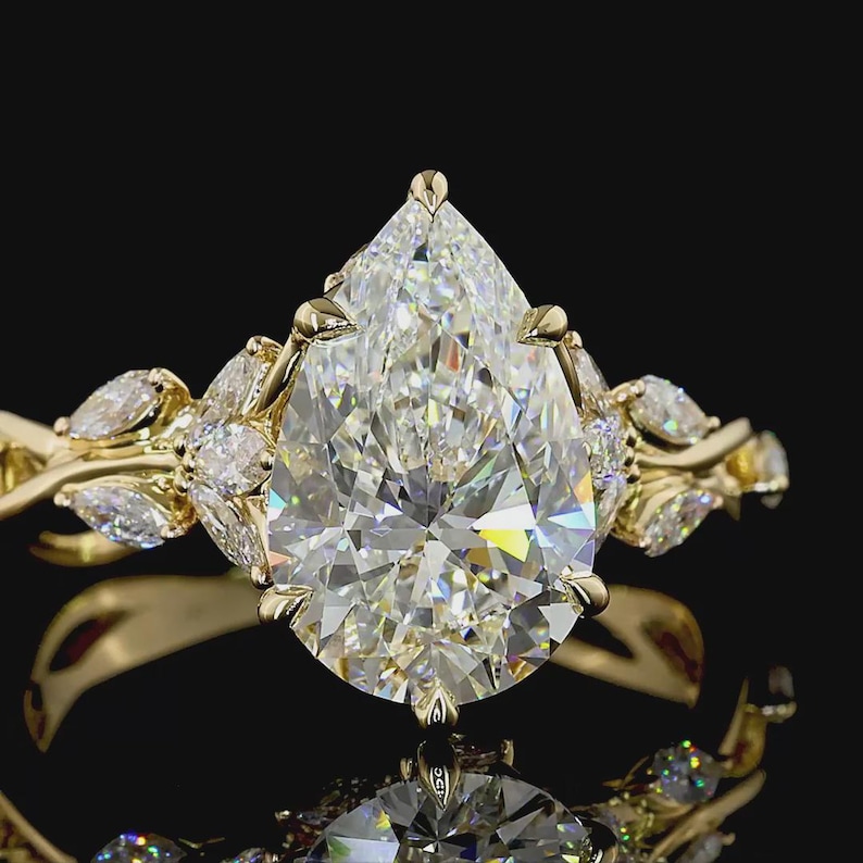 Puede incluir: Un anillo de oro con un gran diamante en forma de pera como pieza central. El anillo est&aacute; adornado con diamantes m&aacute;s peque&ntilde;os con corte marquesa y detalles intrincados en oro, creando un dise&ntilde;o lujoso y elegante. La banda del anillo tiene un dise&ntilde;o floral.