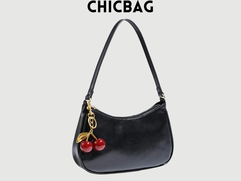 May include: Black shoulder bag with a gold zipper and a cherry charm. The bag has a curved shape and a long strap. The text "CHICBAG" is at the top of the image.
