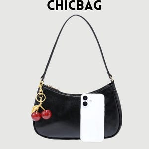 May include: Black shoulder bag with a gold zipper and a cherry charm. The bag has a curved shape and a long strap. The text "CHICBAG" is at the top. A white smartphone is next to the bag.