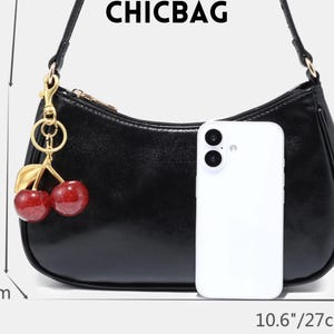 May include: Black shoulder bag with a cherry charm. The bag is 10.6 inches (27 cm) wide, 5.9 inches (15 cm) high, and 2 inches (5 cm) deep. The bag has a gold zipper and a gold cherry charm with red cherries and green leaves. The word CHICBAG is at the top.