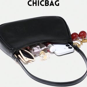 May include: Black handbag with a curved design, open to reveal contents including a smartphone, sunglasses, and perfume bottles. A cherry charm hangs from the strap. The word CHICBAG is printed at the top.