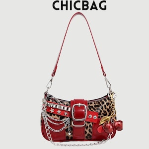 Puede incluir: Un bolso de hombro rojo y con estampado de leopardo con cierre de hebilla y detalles de cadena plateada. El bolso presenta una correa roja y un charm de cereza. El texto "CHICBAG" está en la parte superior.