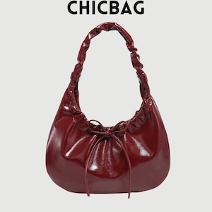 Puede incluir: Un bolso brillante de color burdeos con un asa fruncida y cierre de cordón. El bolso tiene forma de media luna y el texto "CHICBAG" se muestra en la parte superior.