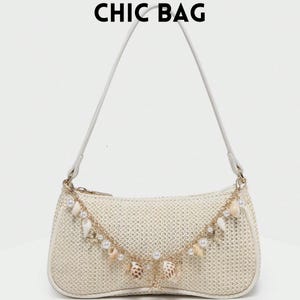 Puede incluir: Bolso de mano tejido de color crema con una correa blanca y herrajes dorados. El bolso está adornado con una cadena decorativa con conchas marinas y perlas. El texto "CHIC BAG" está impreso en la parte superior.
