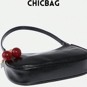 May include: Black shoulder bag with a curved design and a single handle. The bag features a cherry charm with red and gold accents. The word "CHICBAG" is printed at the top.