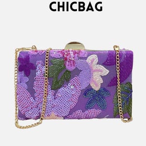 Op de afbeelding: Een rechthoekige paarse clutch met bloemenborduurwerk en pailletten details. De tas heeft een gouden kettingriem en een gouden sluiting. Het woord "CHICBAG" staat bovenaan gedrukt.