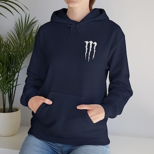 May include: A navy blue hoodie featuring a white Monster Energy logo on the chest. The sweatshirt has a front pocket and a drawstring hood. The long-sleeved top is made of a soft material, suitable for casual wear.